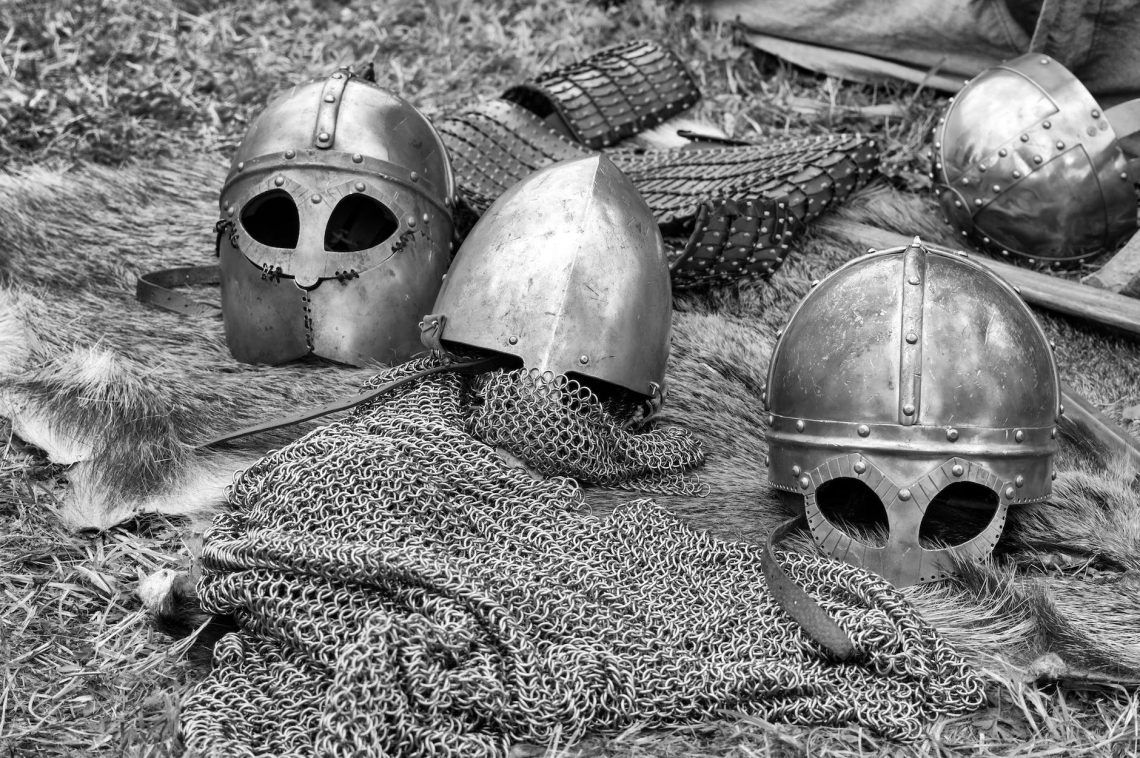 grayscale photography of chainmails and helmets on ground